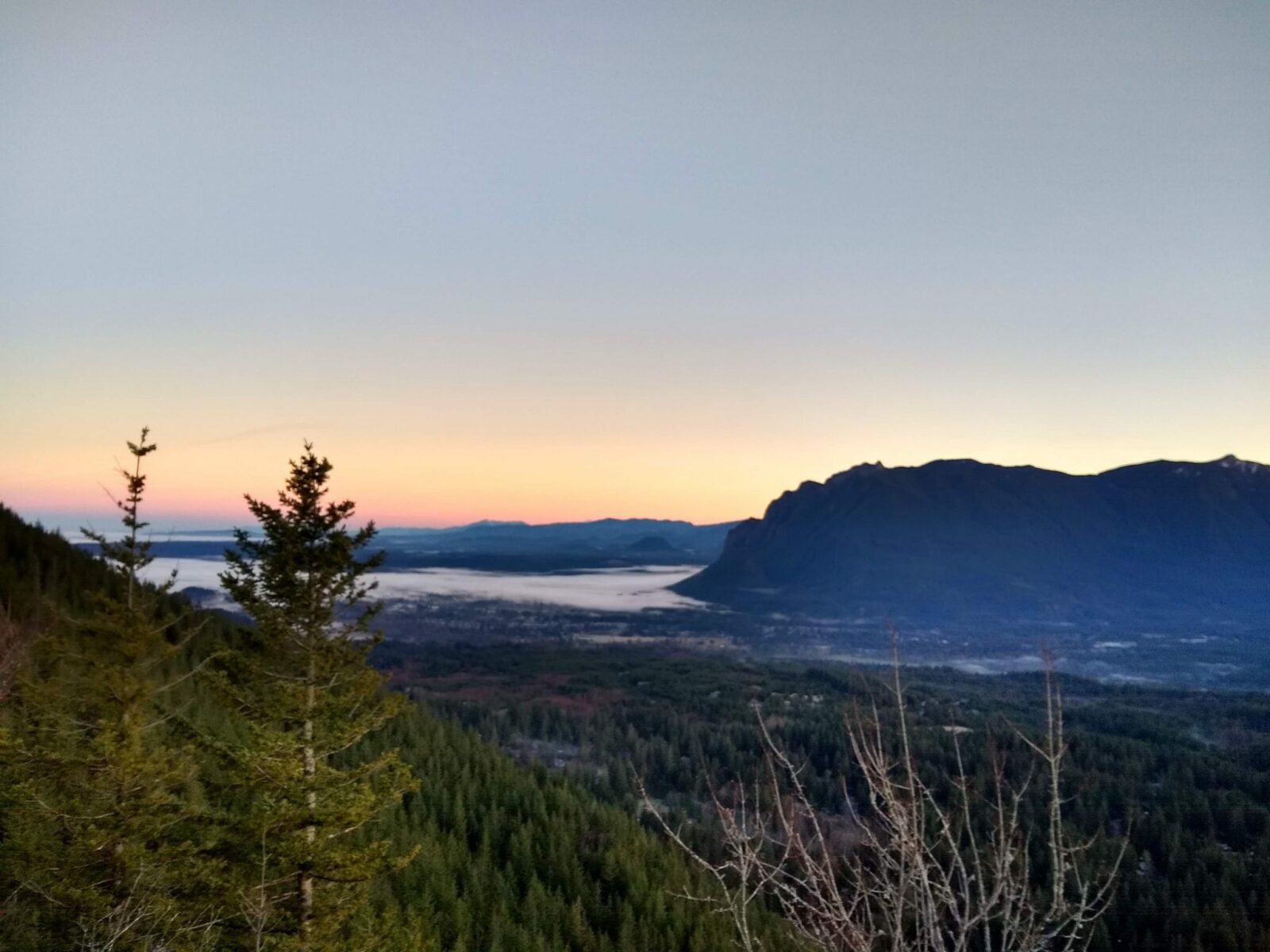 sunrise sky with mountains, a valley and trees in the foreground