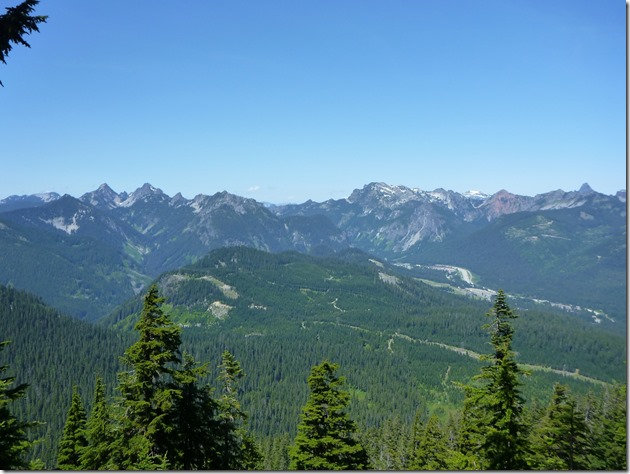 Tall mountains in the distance, smaller mountains and evergreen trees in the foreground