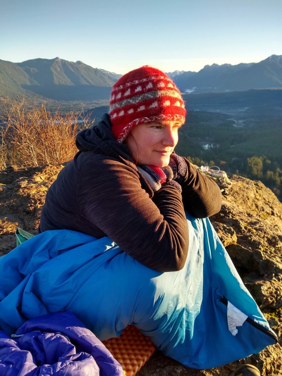 Woman in a hat and sleeping bag sitting on a rock