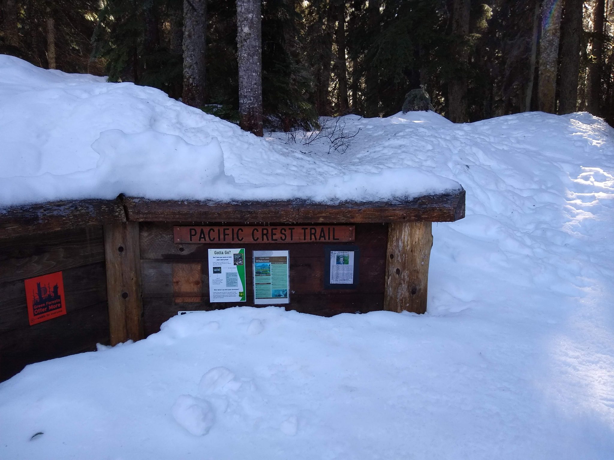 Trail sign for Pacific Crest Trail partially covered with deep snow