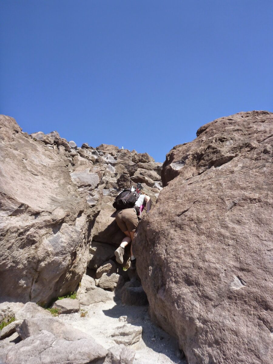 hiker climbing between two large boulders against a blue sky