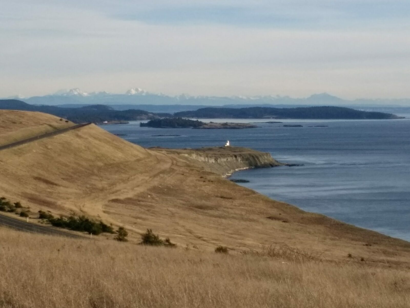 A field along a beach with a lighthouse and distant islands and mountains on San Juan Island, one of the beste weekend getaways from Seattle