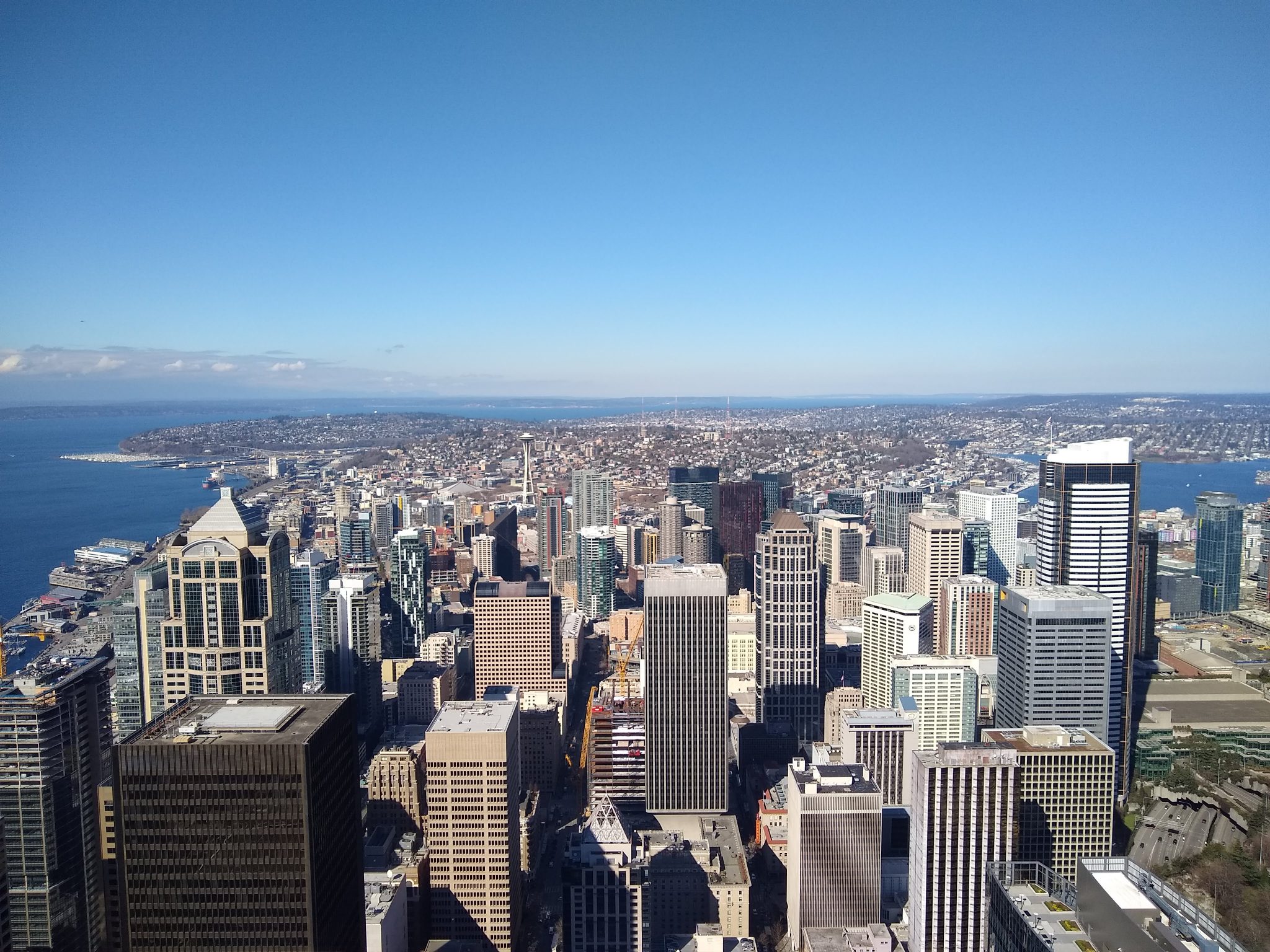 A city seen from a high building, with water and a few clouds against a blue sky