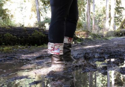 A big mud puddle with a woman's legs. She is wearing rubber boots and black leggings