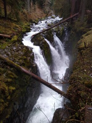 A waterfall with three falls coming down from a river above to a canyon below