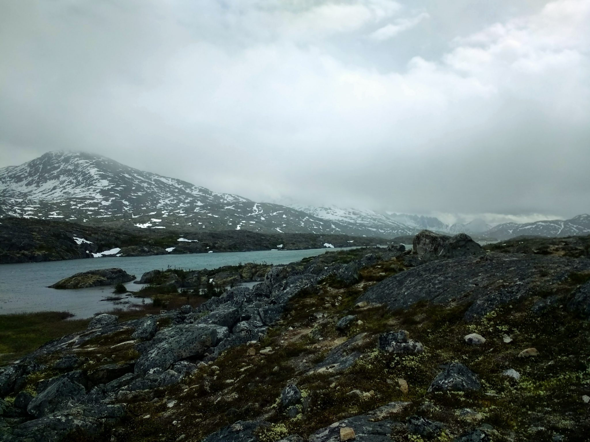 An alpine lake and rocks with mountains covered in fog