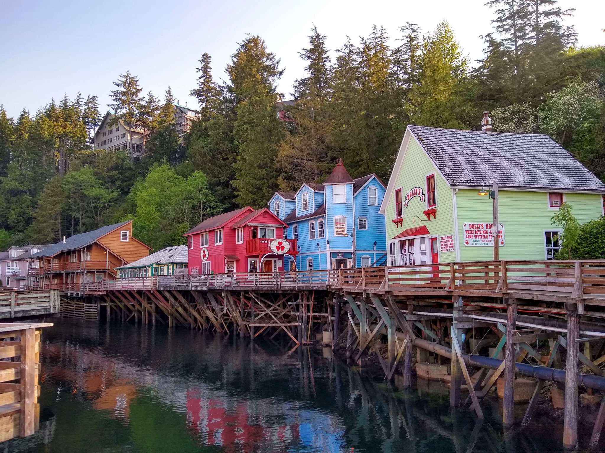 Brightly colored historic buildings are built on stilts against evergreen trees along Creek Street in Ketchikan, Alaska