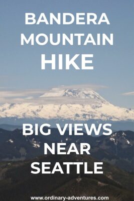 Mt Rainier, a high snow covered mountain, in the background surrounded by a few clouds on an otherwise sunny day. Smaller mountains are in the foreground. Text reads: Bandera Mountain hike, big views near Seattle