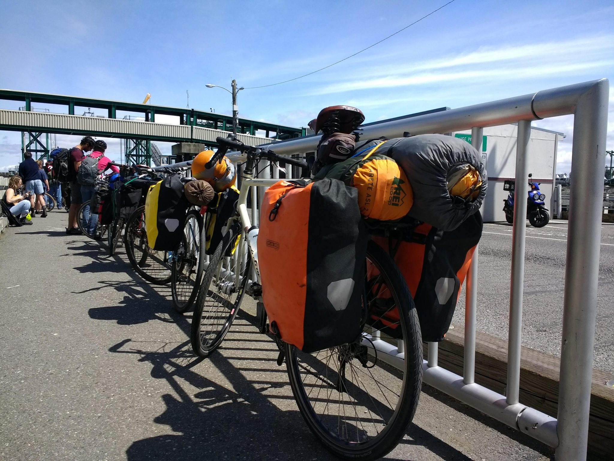 A group of bikes loaded with colorful camping gear next to a metal barrier on a dock, getting ready for Lopez Island bike camping