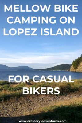 Lopez Island bike camping at Spencer Spit State Park. There is a grassy spit in the foreground wtih a canoe, tideflats and water behind. Forested islands are in the background on a sunny day. Text reads: Mellow bike camping on lopez island for casual bikers