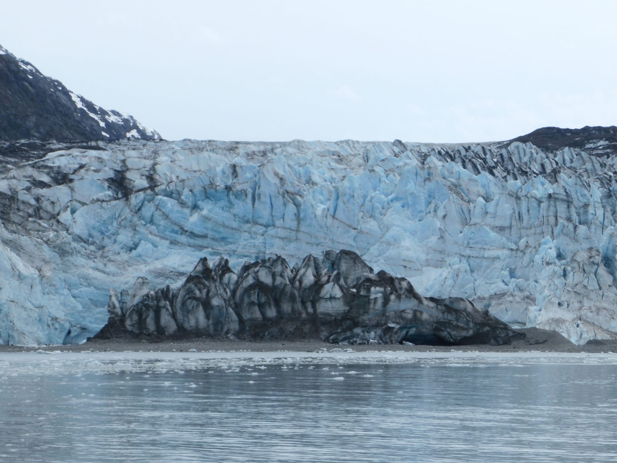A glacier touches the sea in Glacier Bay. There is blue ice and in front of it the ice is gray and black where it is filled with rocks and gravel
