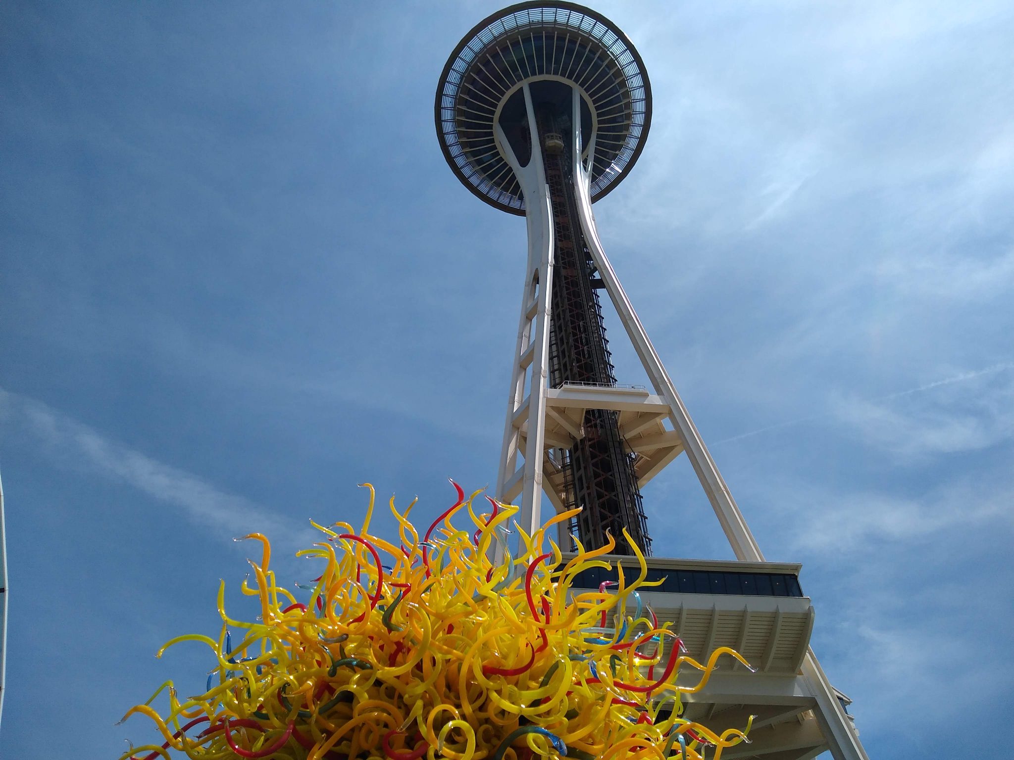 A view of the Space Needle from below on a sunny day. There is a yellow and red glass sculpture below it