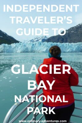 A woman stands at the back of a boat facing away from the camera. She is looking at the blue ice of a glacier and mountains behind it. In the foreground there are lots of small pieces of ice in the water on a visit to Glacier Bay national park