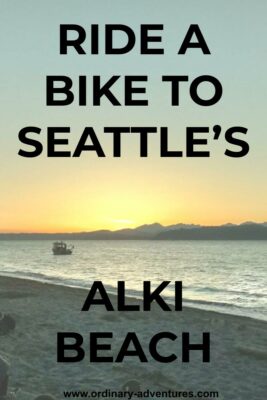 A sunset behind mountains. In the foreground is water and a beach, with a single fishing boat. Text reads: Ride a bike to Seattle's Alki beach