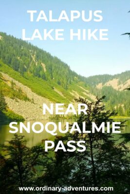 Talapus lake hike near Snoqualmie pass. It's a large alpine lake surrounded by forest and rocky mountains, which are reflected in the lake. There are evergreen trees in the foreground and it's a sunny day. Text reads: Talapus lake hike near snoqualmie pass