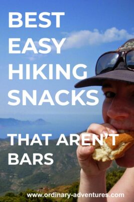 A person eating some bread on a hike. They have a hat and sunglasses. There is blue sky and a landscape beyond of mountains and water. Text reads: Best easy hiking snacks that aren't bars