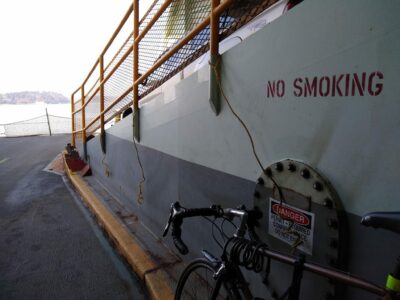 Against the wall on the deck of a ship there is a bike tied by a yellow rope.