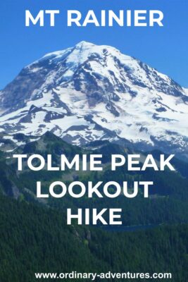 The Tolmie Peak Lookout hike has epic views of Mt Rainier. Here it is filling the frame against a clear blue sky with forested hillsides in the foreground. Text reads: Mt Rainer Tolmie peak lookout hike