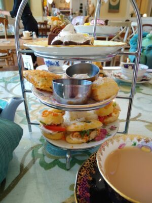 A tiered tray in a restaurant with a variety of sandwiches and pastries on a table. There is also a cup of tea in a china cup.
