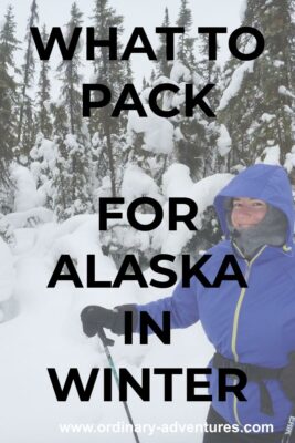 A person holding ski poles and dressed in lots of warm clothes on a snowy day in the forest. The person is smiling. Text reads: What to pack for Alaska in winter