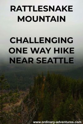 On the Rattlesnake Mountain hike, a view down to Rattlesnake Ledge, a popular hiking destination. In the foreground are evergreen trees, in the background there are low clouds covering the mountains and clinging to the middle fork snoqualmie river valley. Text reads: Rattlesnake mountain, challenging one way hike near seattle