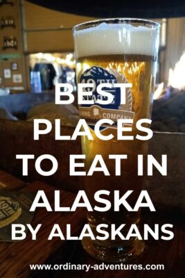 A beer in a pint glass on a wooden table in a restaurant in Alaska. Text reads: Best places to eat in Alaska by Alaskans