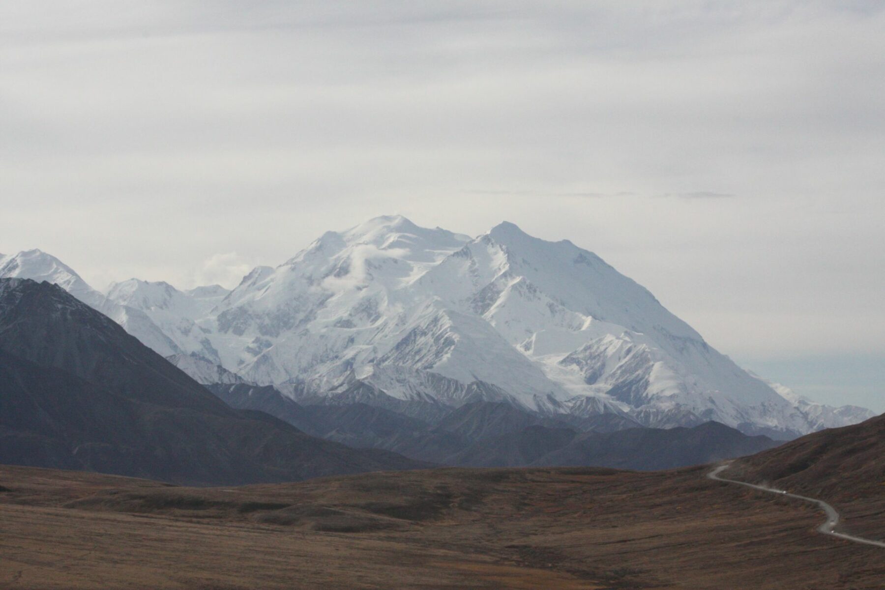 Denali, the High One, is seen across a valley in Denali National Park, a popular Alaska National park. There is a road following the valley.