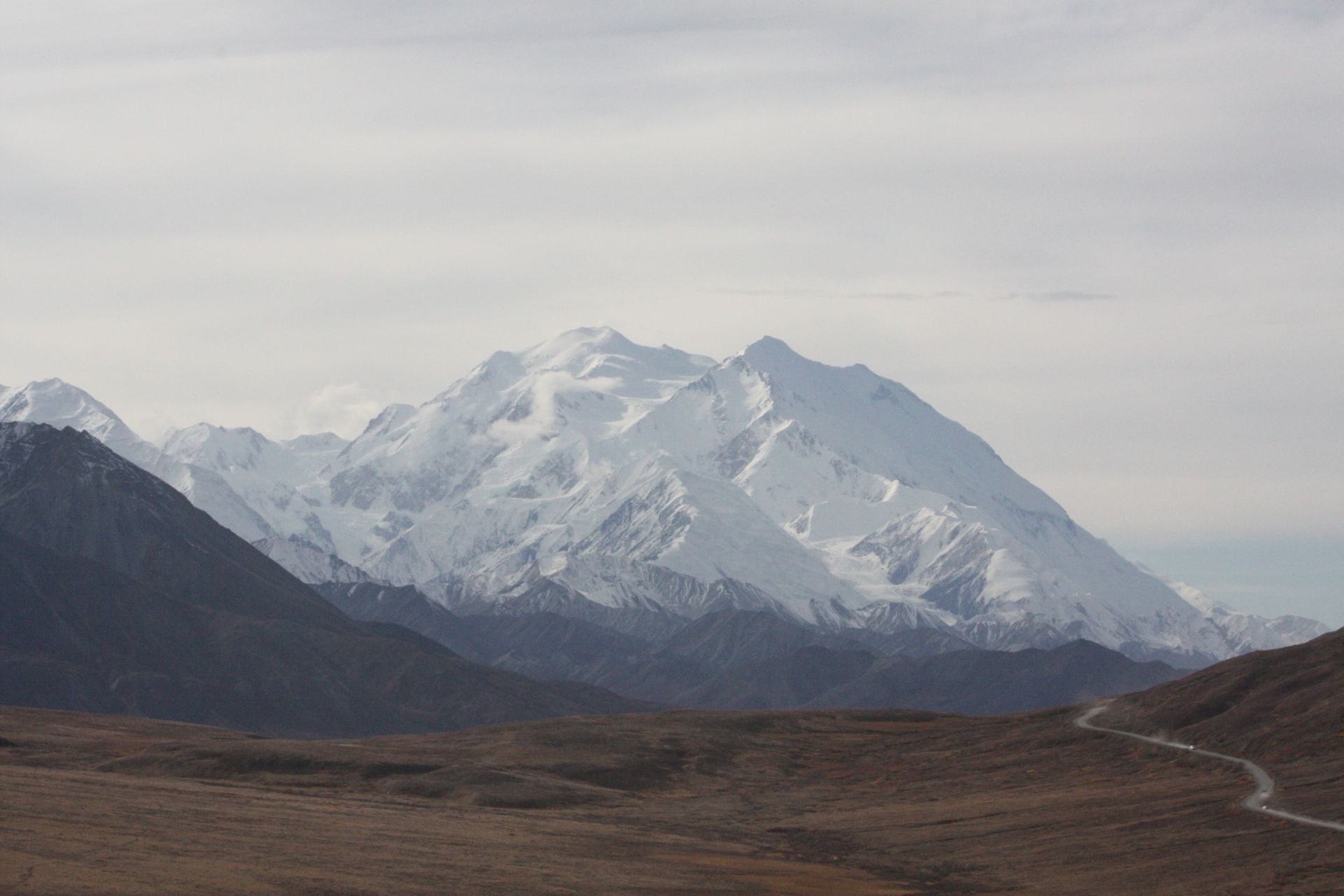 Denali, the highest mountain in North America, rises above a valley and the park road in Denali National Park