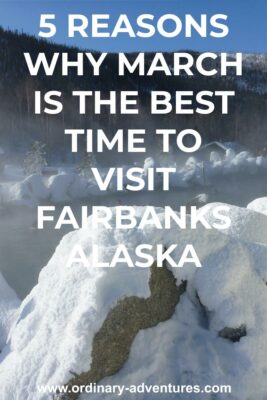 A hot springs pool is surrounded by rocks covered in snow. There is steam coming up from the pool. There are a few log buildings nearby and the area is surrounded by forested hills. Text reads 5 reasons why March is the best time to visit Fairbanks Alaska