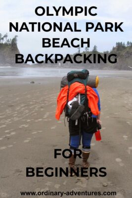 A person wearing rubber boots walks down the beach with a large backpack. The backpack holds a tent and an orange rain jacket. In the distance are cliffs and trees surrounding the beach.