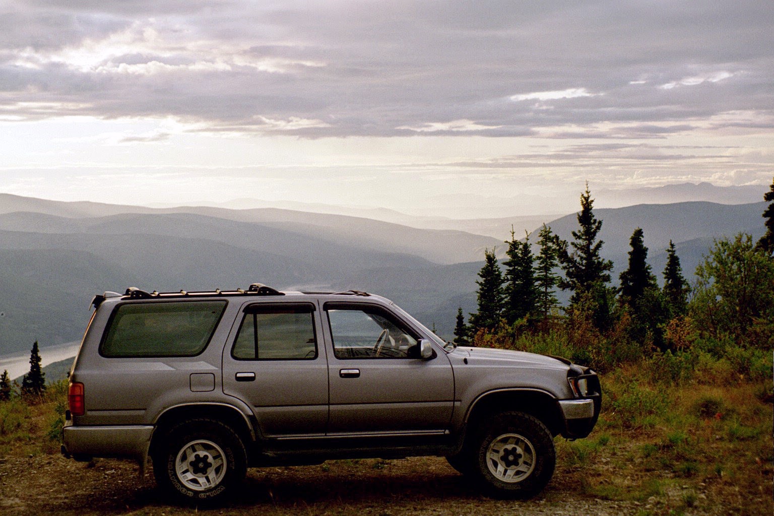 when you plan a road trip, make sure to get your car ready! An older gray SUV is parked on a high hill above a river.