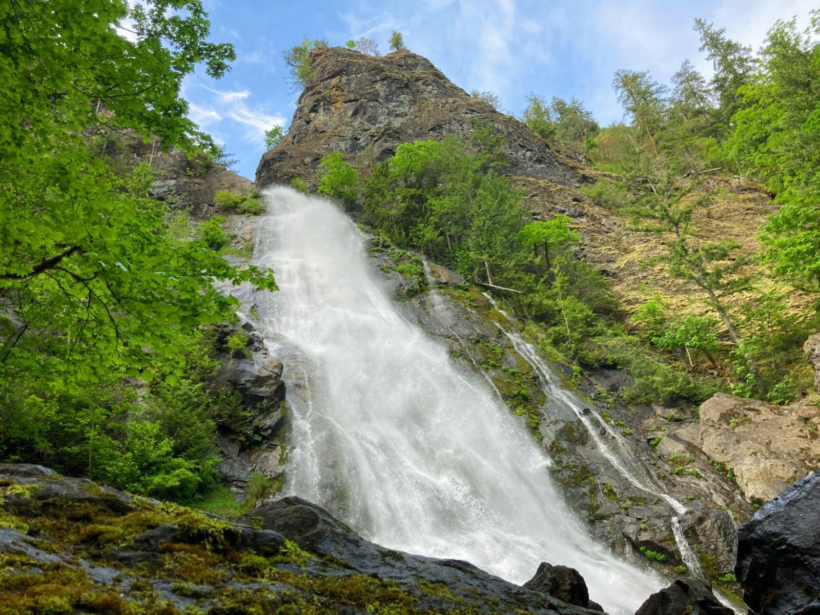 A wide waterfall seeing from below coming over a boulder field with rocks and trees on each side