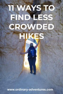 A hiker stands in a hole in a rock. She has one arm to the side and one above her head. There is bright sunlight on the other side of the hole. Text reads: 11 ways to find less crowded hikes