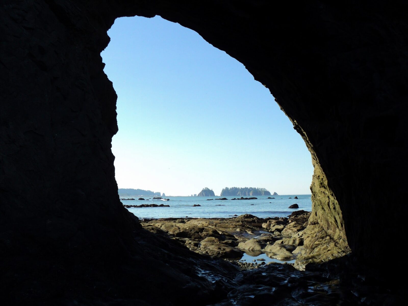 A large hole in a rock on the beach in Olympic National Park. Tidepools are under the arch and distant islands can be seen in the ocean in the distance