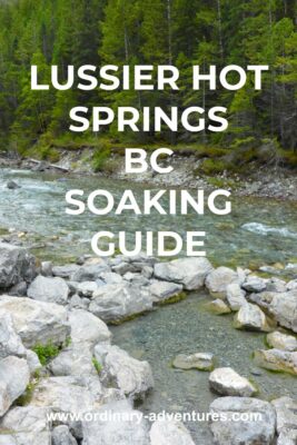 Lussier Hot Springs is a series of three pools next to a river. In the foreground is a hot pool surrounded by rocks. Behind the rocks the river flows by. The river is flowing through an evergreen forest between mountains. Text reads; Lussier Hot Springs BC Soaking guide