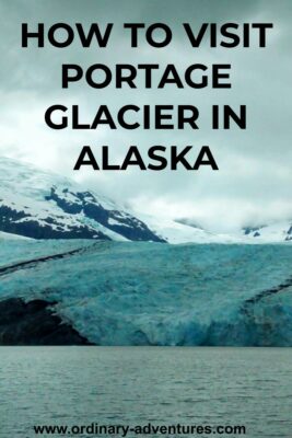 Blue ice at the foot of a glacier touching a lake. There are mountains and more ice behind on an overcast day. Text reads: how to visit portage glacier in Alaska