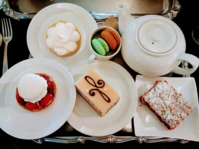 A white teapot and four white plates are on a silver tray. Each plate has a pastry on it and there is a small bowl with two macarons at Murchie's, an excellent alternative to traditional afternoon tea in Victoria BC