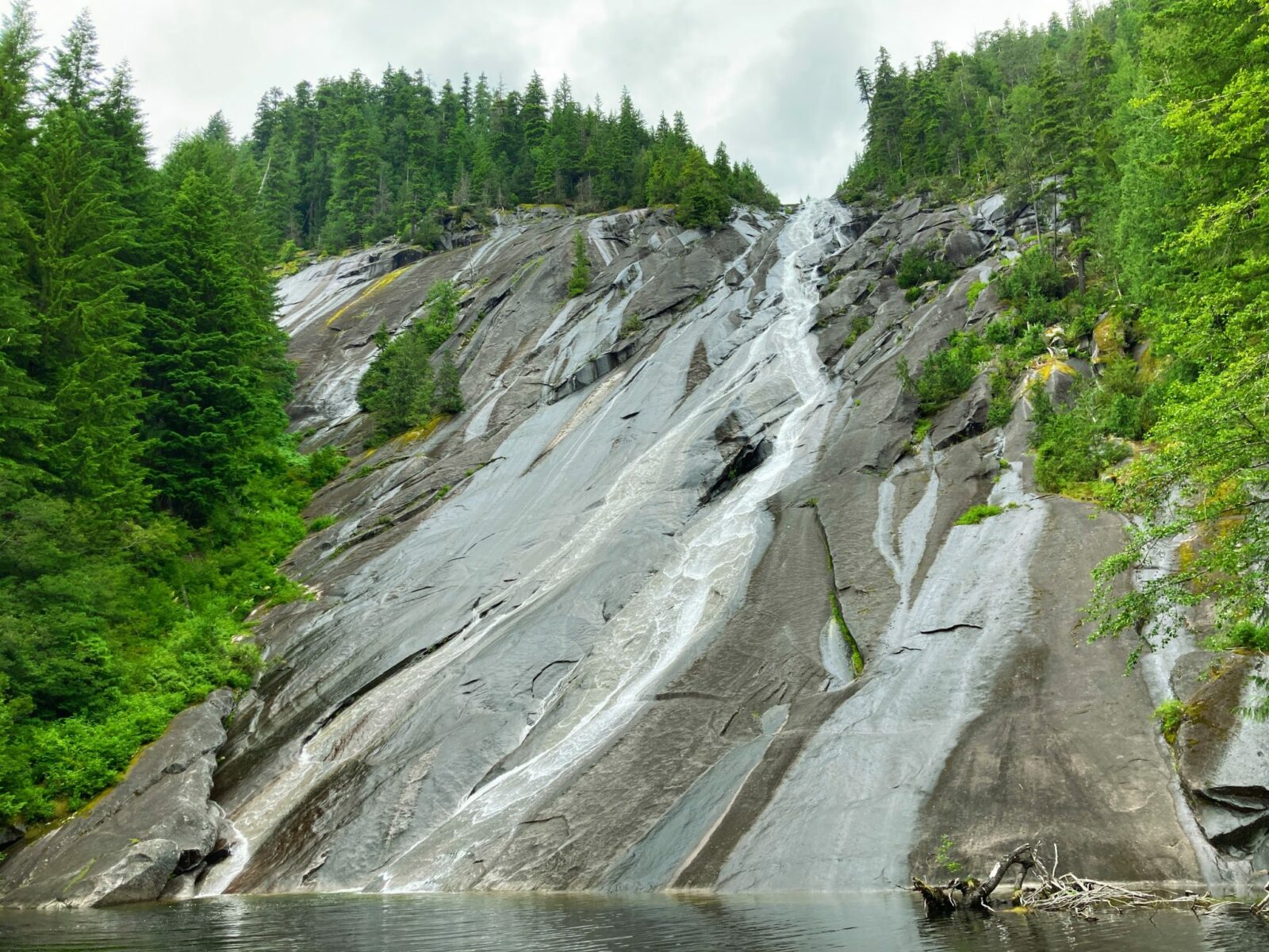 Otter Falls, one of the longer hikes near north bend, spills over a high rock and then spreads out over the flat surface of a rock next to a small lake. The giant rock face is surrounded by evergreen trees