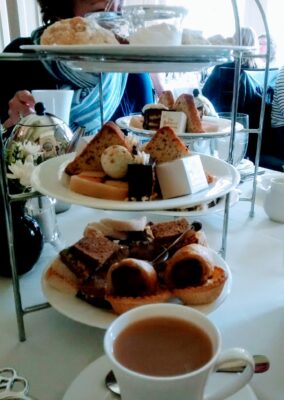 A traditional tea tray at afternoon tea in Victoria, BC. The tray has three white tiers, each with sandwiches and pastries. There is a cup of tea on a saucer next to the tea tray