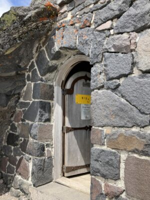 A rock walk with a rounded wooden door. The wooden door is open. The wall is built along the side of the rocks on the Skyline Trail in Mt Rainier National Park