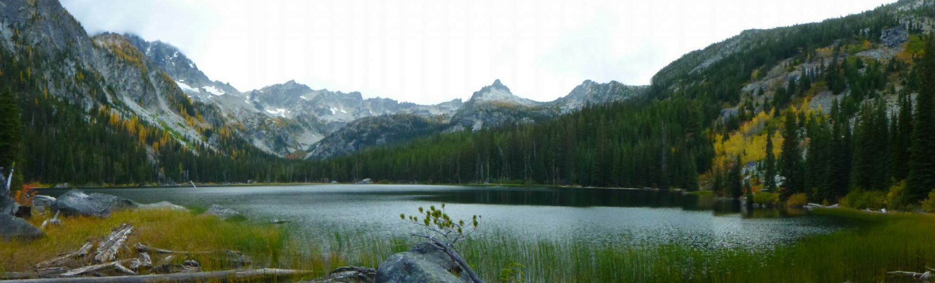 Lake Stuart surrounded by grasses, evergreen trees, golden larches and high distant mountains