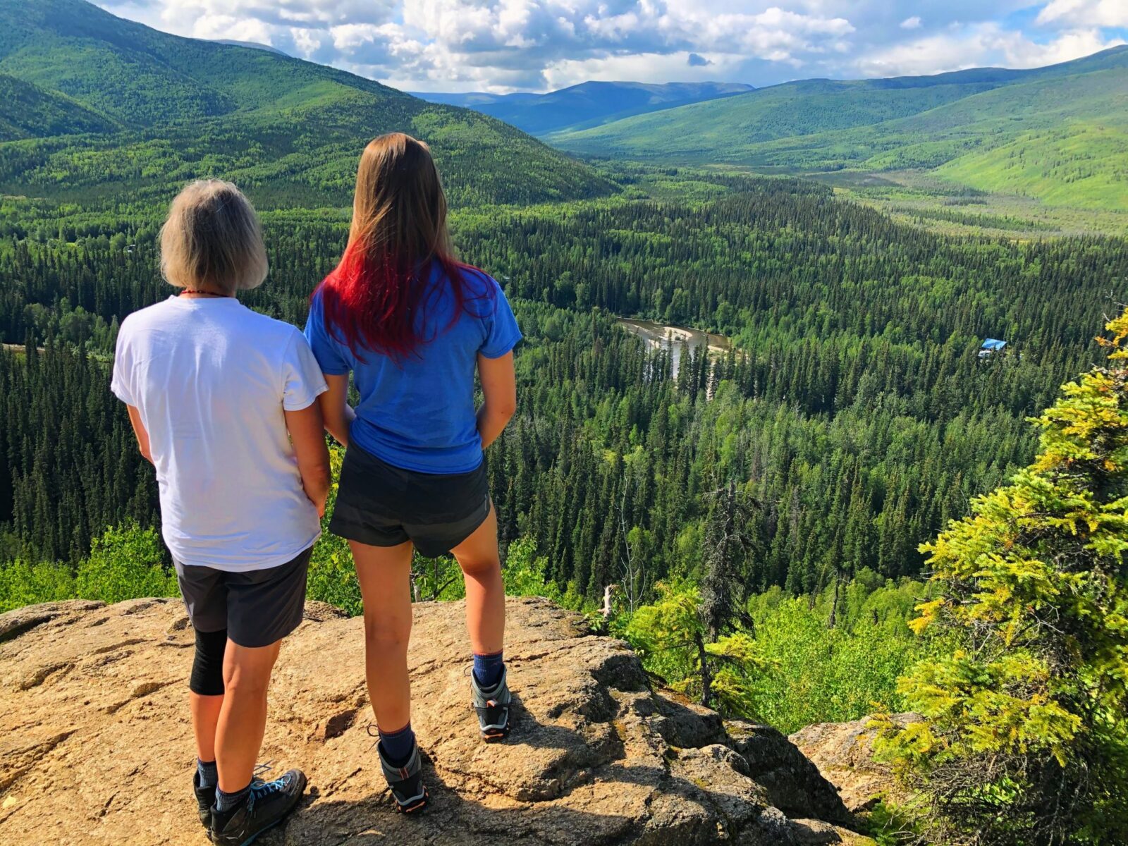 Two hikers admire the view of forested hillsides and a river below on a partly cloudy day from the angel rocks trail