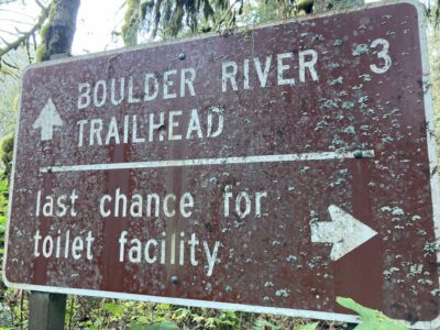 A brown national forest service sign points ahead for the boulder river trailhead in three miles and the last chance toilet facility with an arrow pointing right