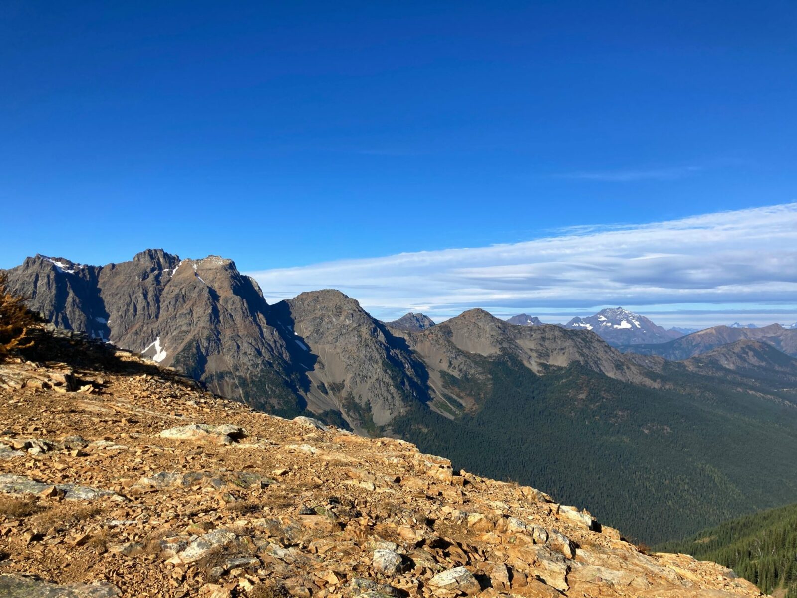 Several high mountains with a bit of lingering snow with a rocky ledge in the foreground along the Pacific Crest Trail on the way to Grasshopper Pass