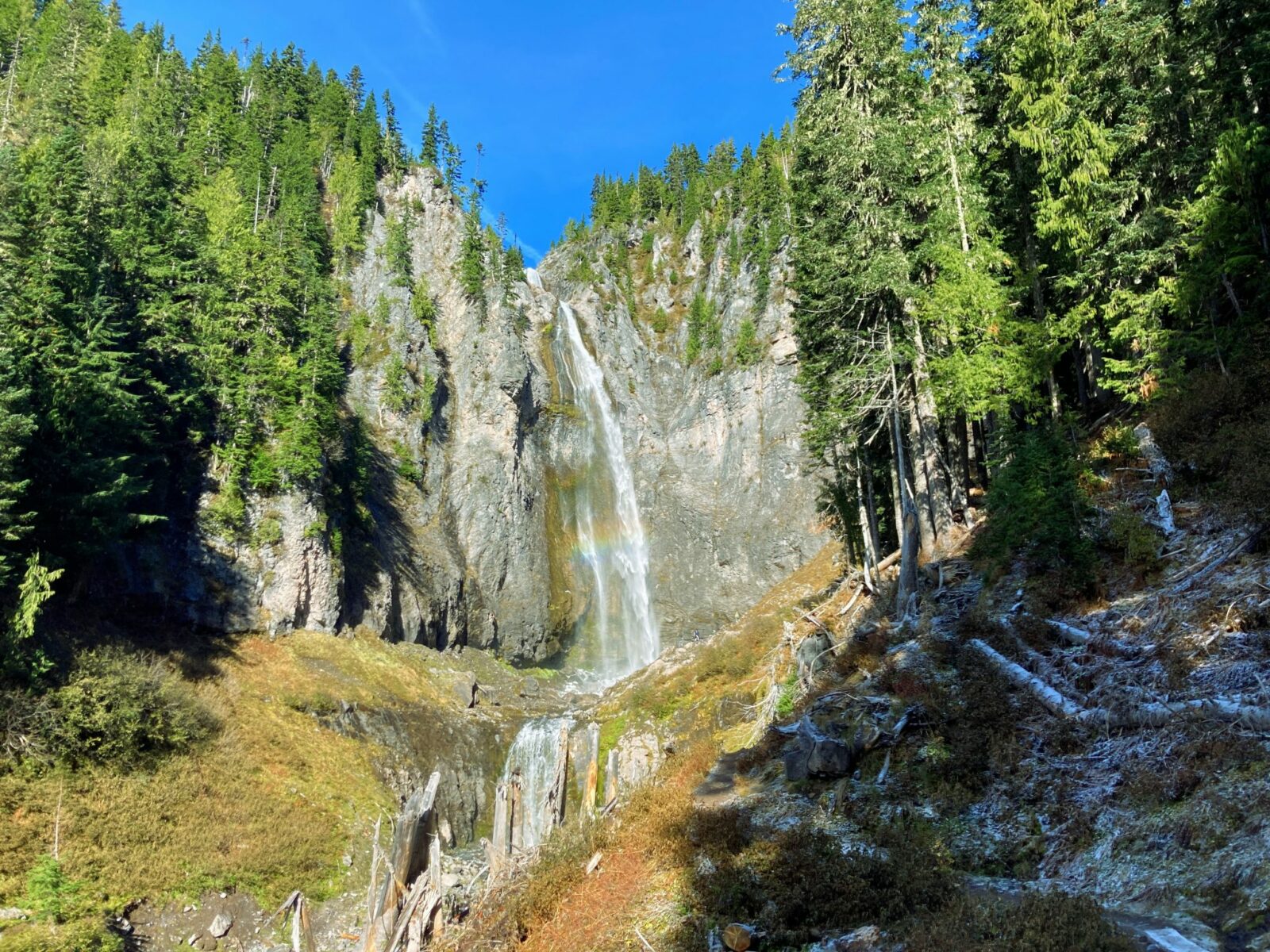 Comet Falls comes straight down a cliff face with forests around the cliff on a sunny day