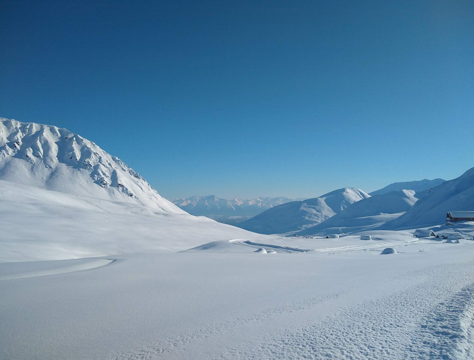Hatcher Pass in Alaska in winter. There is a giant snowy valley surrounded by mountains on a snowy day. There are even higher mountains in the distance