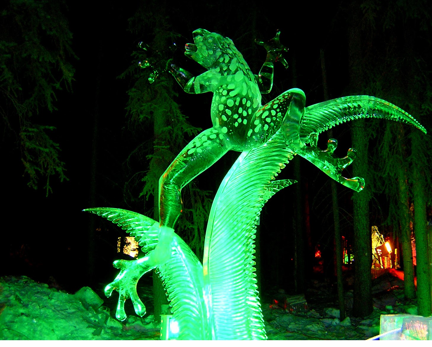 A giant frog carved from ice. It is dark and the frog is lighted in green lights.