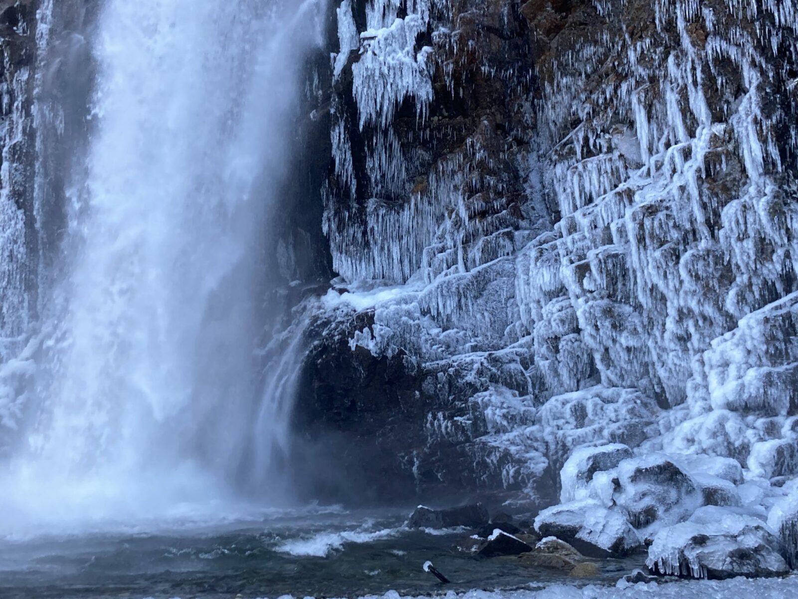 Franklin Falls in winter splashing into a pool at the base of the falls. The rocks are covered in ice and icicles around the waterfall base