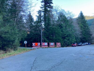 Closed road signs across a road where you park to hike Franklin Falls in winter from the Denny Creek side. There are cars parked along the road and trees around the road.