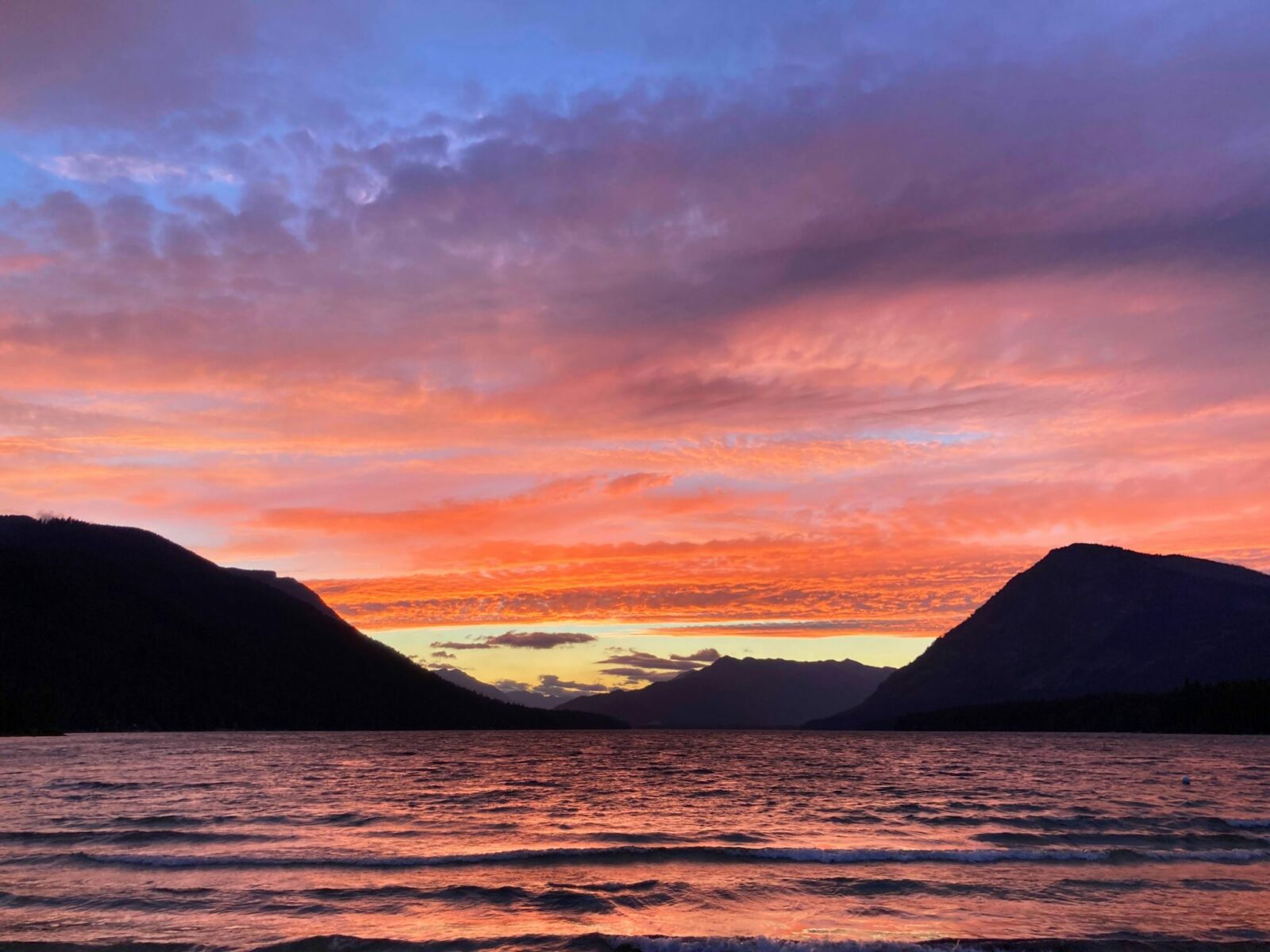 A pink and orange summer sunset behind mountains across a large alpine lake.